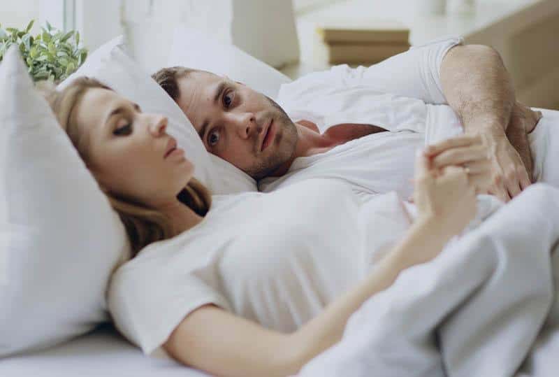 Couple allongé sur un lit, échangeant un regard complice